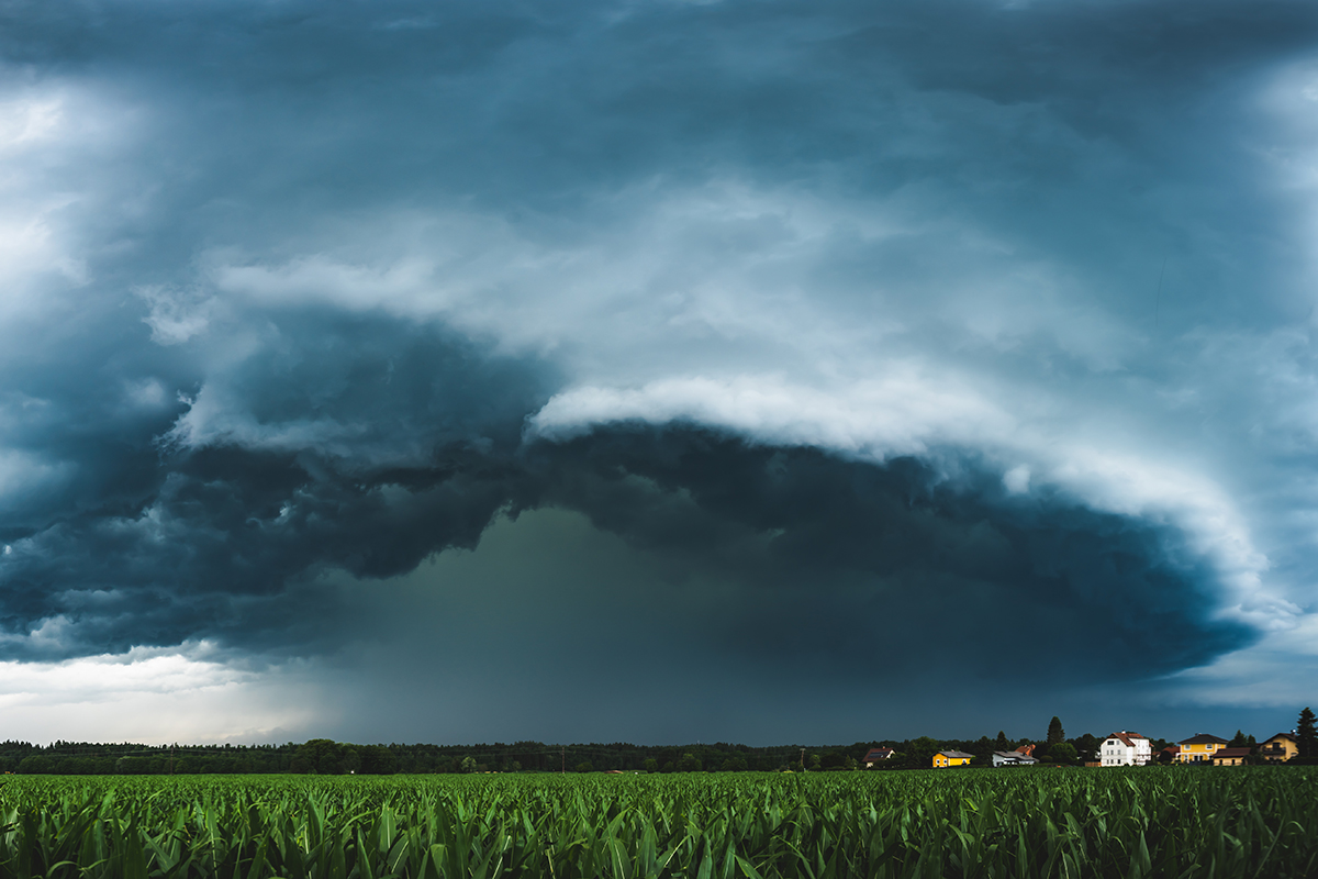 Panoramic view of a terrifying dark thunderstorm approaching small village. Flowing above corn fields.